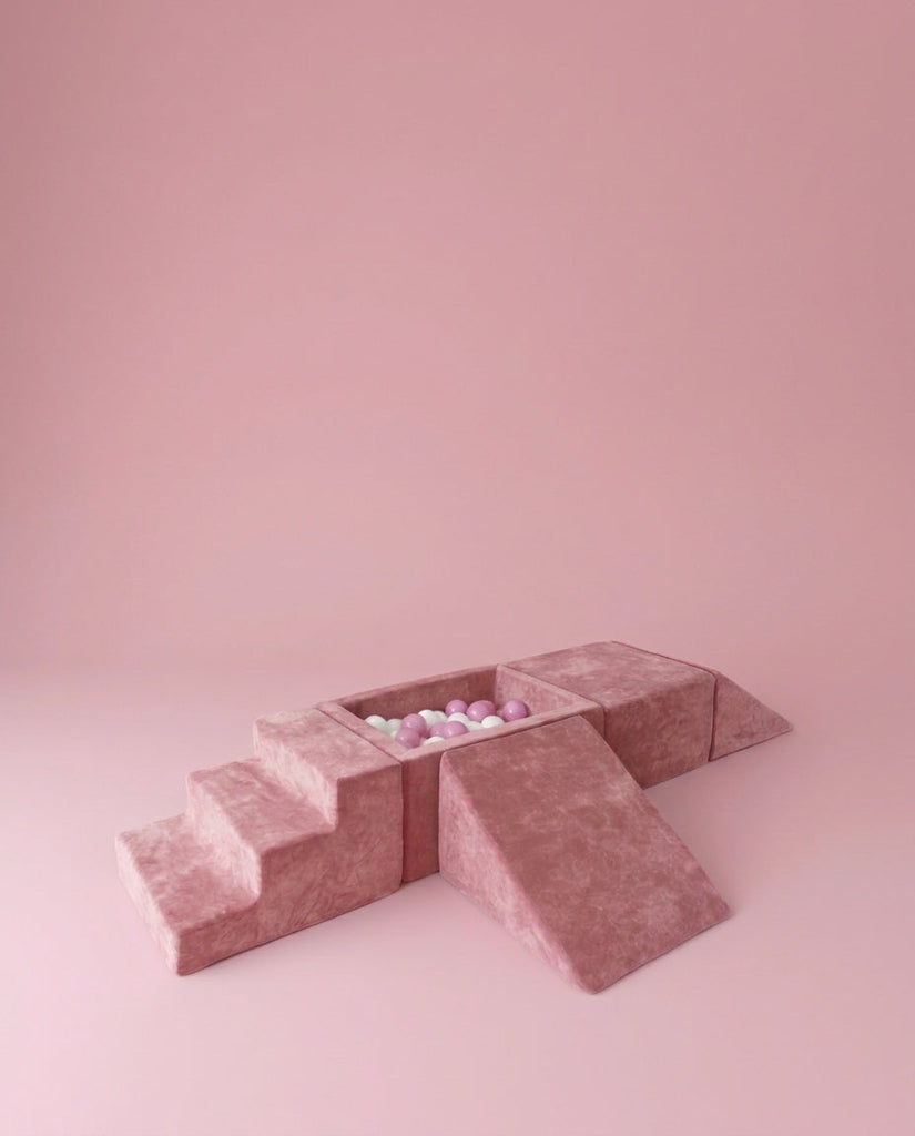 Roze foam speelelementen met een trap, helling en ballenbak met witte, roze en lichtgroene ballen op een roze ondergrond.