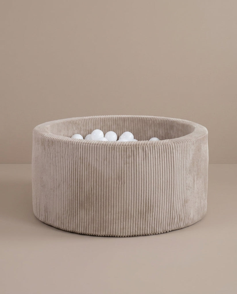 Rond beige ballenbad met ribstructuur en witte ballen op een beige ondergrond.