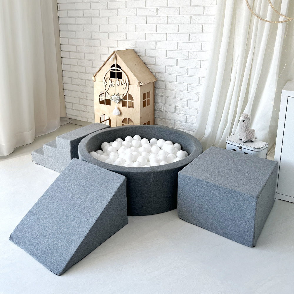 Grijs rond ballenbad met witte ballen, een grijs trapje, een helling en een kubusvormig blok in een speelkamer.