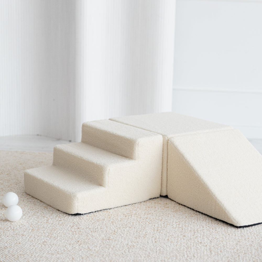 Crèmekleurige bouclé speelset van dichtbij, met een trapje naast een blok en een helling.