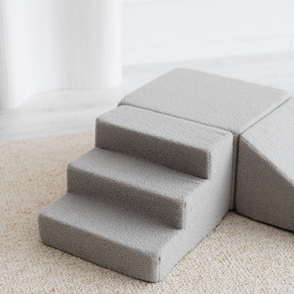 Detail van het grijze bouclé trapje met drie treden, naast het blok en de helling van de speelset.