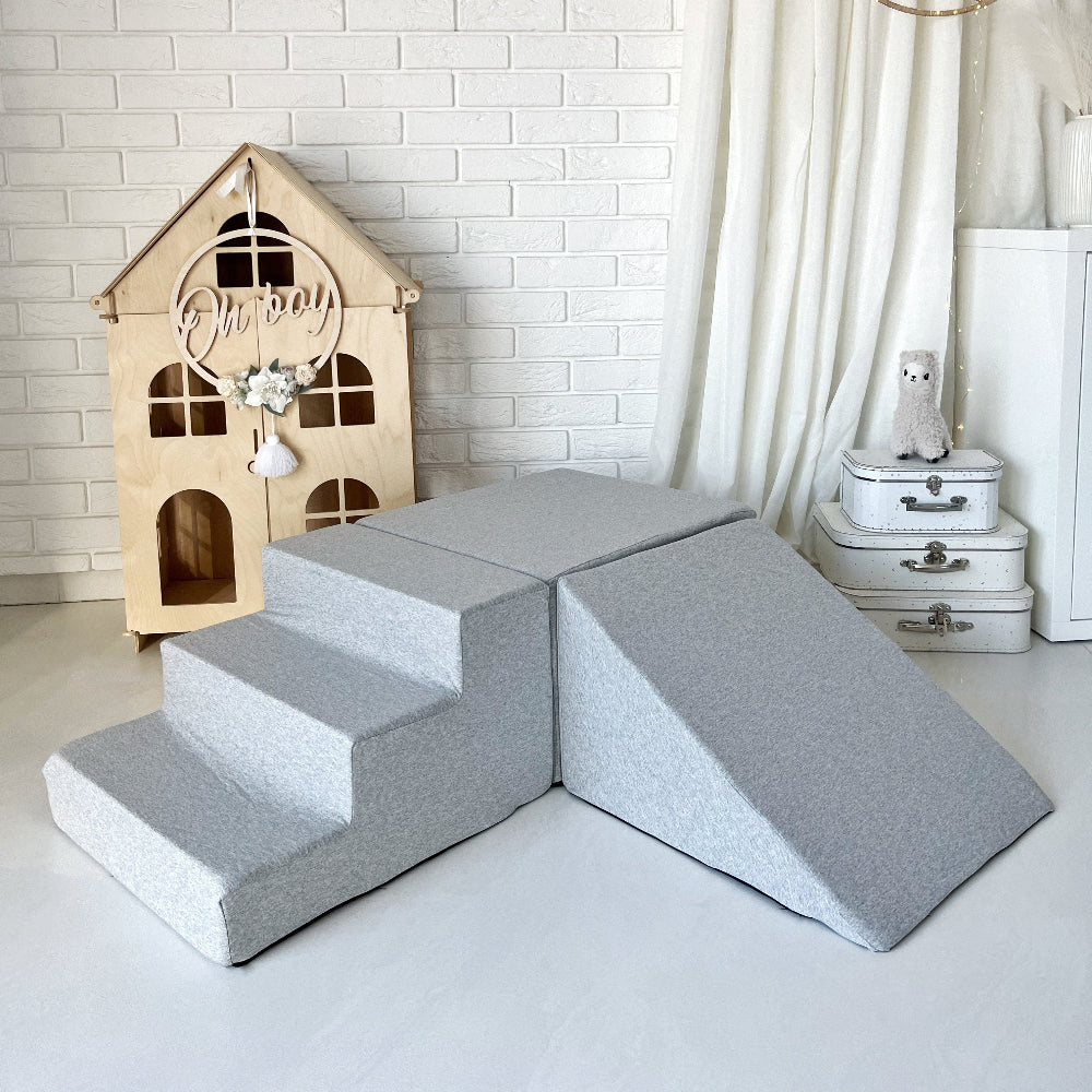 Lichtgrijze driedelige speelset met trapje, rechthoekig blok en helling naast een houten speelhuis.
