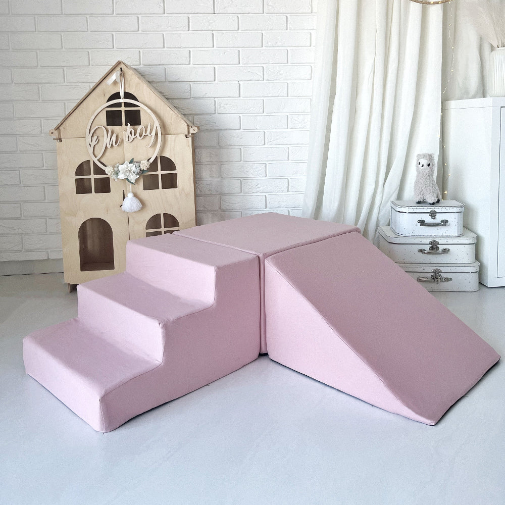 Roze speelset met drie elementen: een trapje, rechthoekig blok en helling, opgesteld in een kinderkamer.