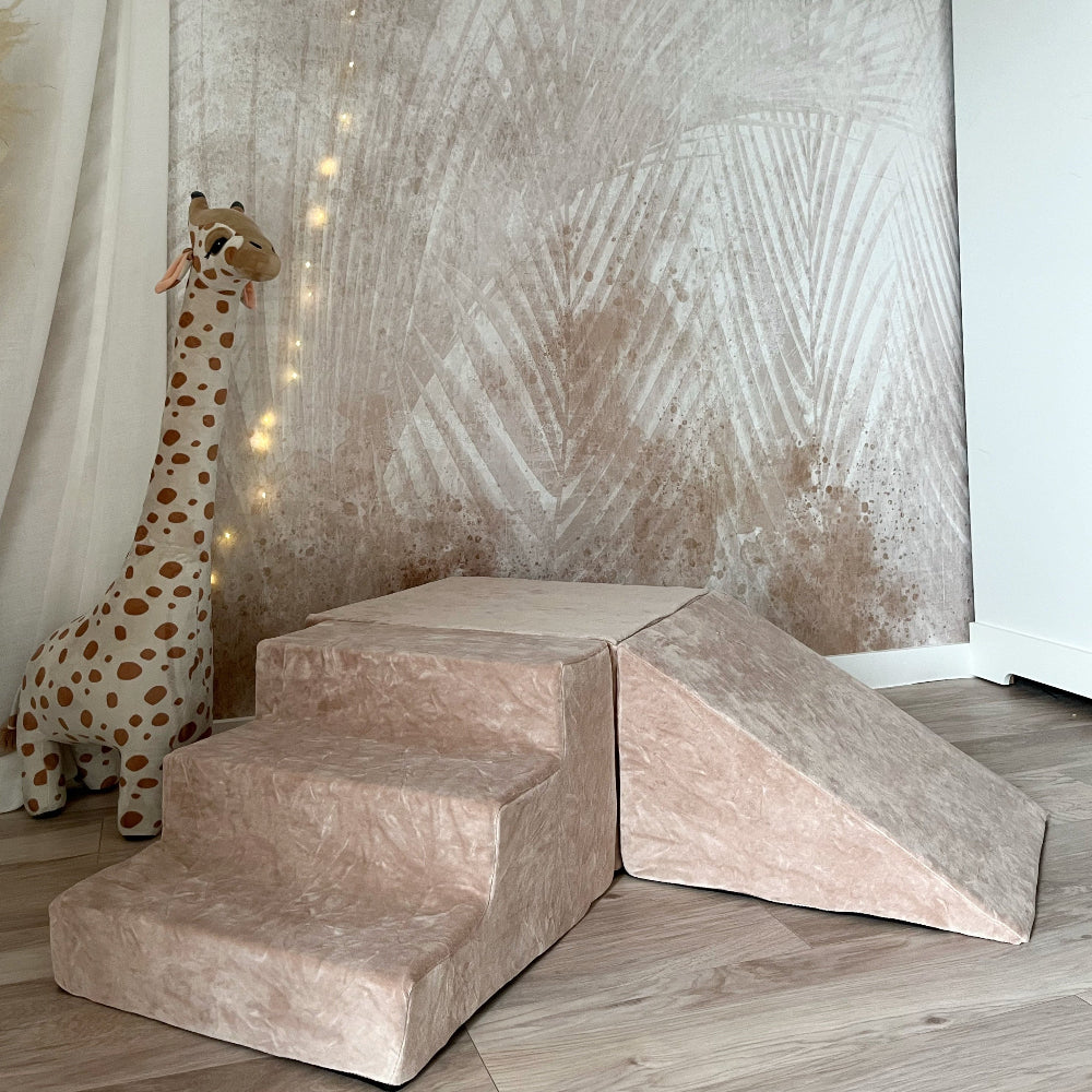 Donkerbeige velours speelset met een trapje vooraan, een blok erachter en een helling rechts, naast een pluchen giraf.