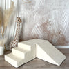 Ecru Soft Velvet speelset in hoekopstelling met trapje linksvoor, blok achteraan en helling rechts, naast een girafknuffel.