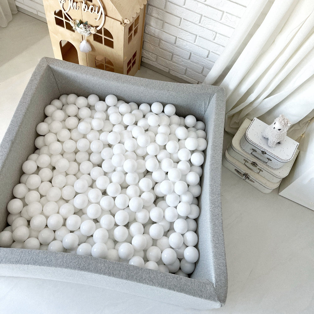 Vierkant lichtgrijs ballenbad met witte en licht crèmekleurige balletjes in een kinderkamer.