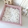 Vierkant roze ballenbad met witte balletjes in een kinderkamer, van bovenaf gezien.