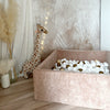 Vierkant donkerbeige velours ballenbad met witte, goudkleurige en beige balletjes naast een pluchen giraf.