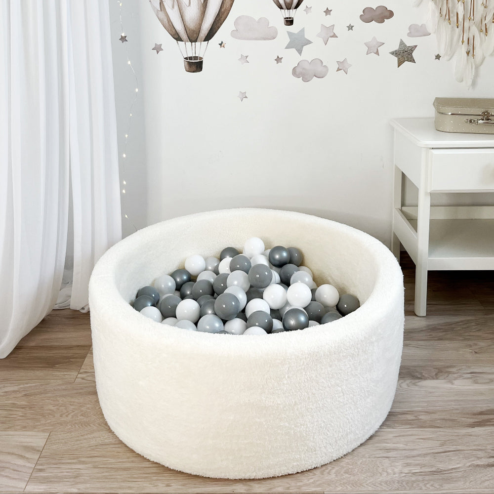 Rond wit teddy ballenbad met witte en grijze ballen op een houtkleurige vloer in een kinderkamer.