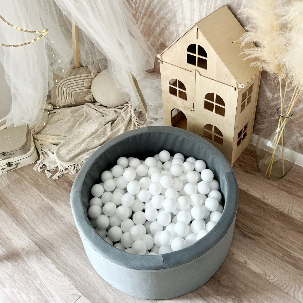 Rond grijs ballenbad met witte balletjes, van bovenaf gezien naast een houten poppenhuis.