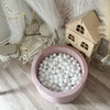 Lichtroze ballenbad met witte balletjes van bovenaf gezien, naast een houten speelhuisje en een speelhoek met klamboe.