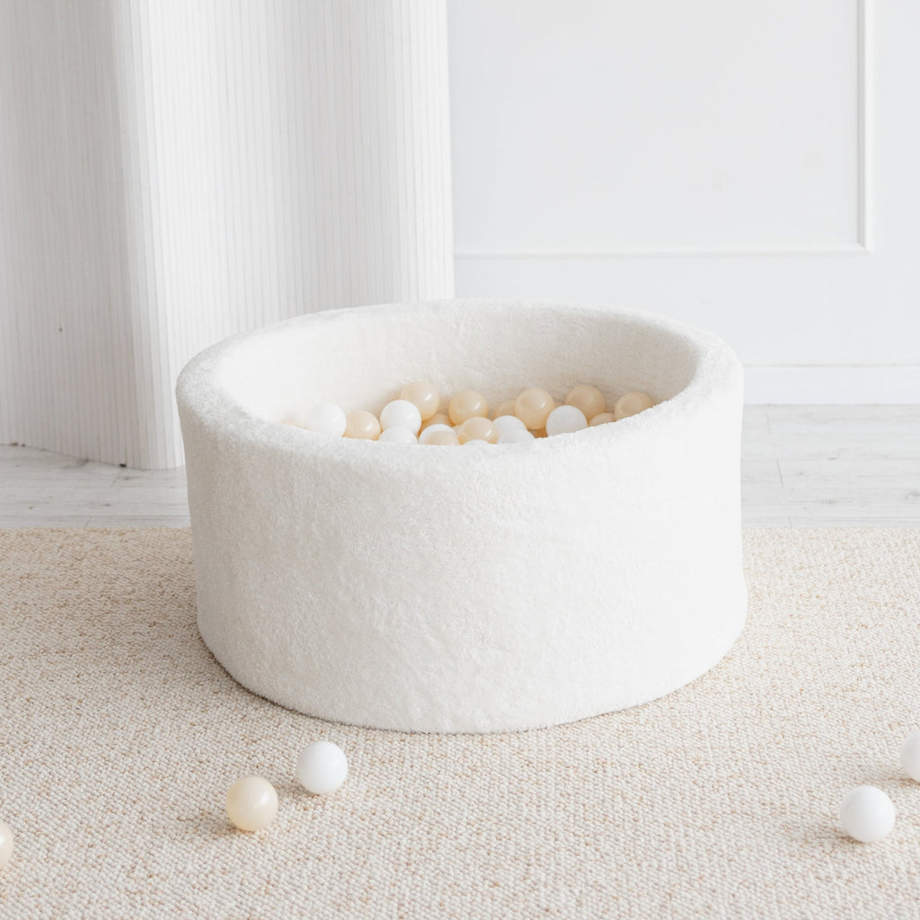 Rond wit teddy ballenbad met witte en crèmekleurige balletjes op een licht vloerkleed, met enkele balletjes ernaast.