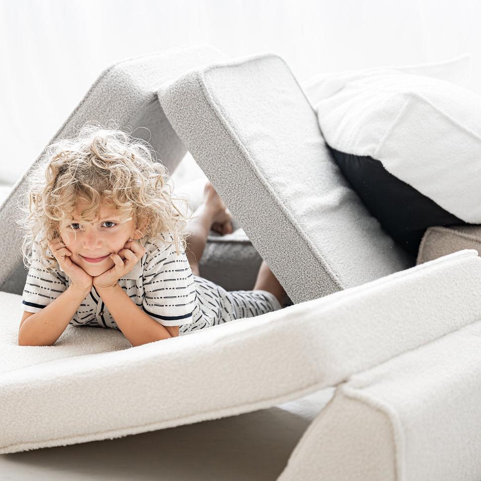 Kind ligt op de crèmekleurige bouclé lounger onder twee schuin tegen elkaar geplaatste segmenten.