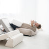 Kind ligt achterover op een lounger tussen speelkussens, met de witte bouclé lounger op de voorgrond.