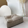 Beige bouclé ottoman kinderpoef met vierkante vorm en opstaande naden op een lichte vloer.