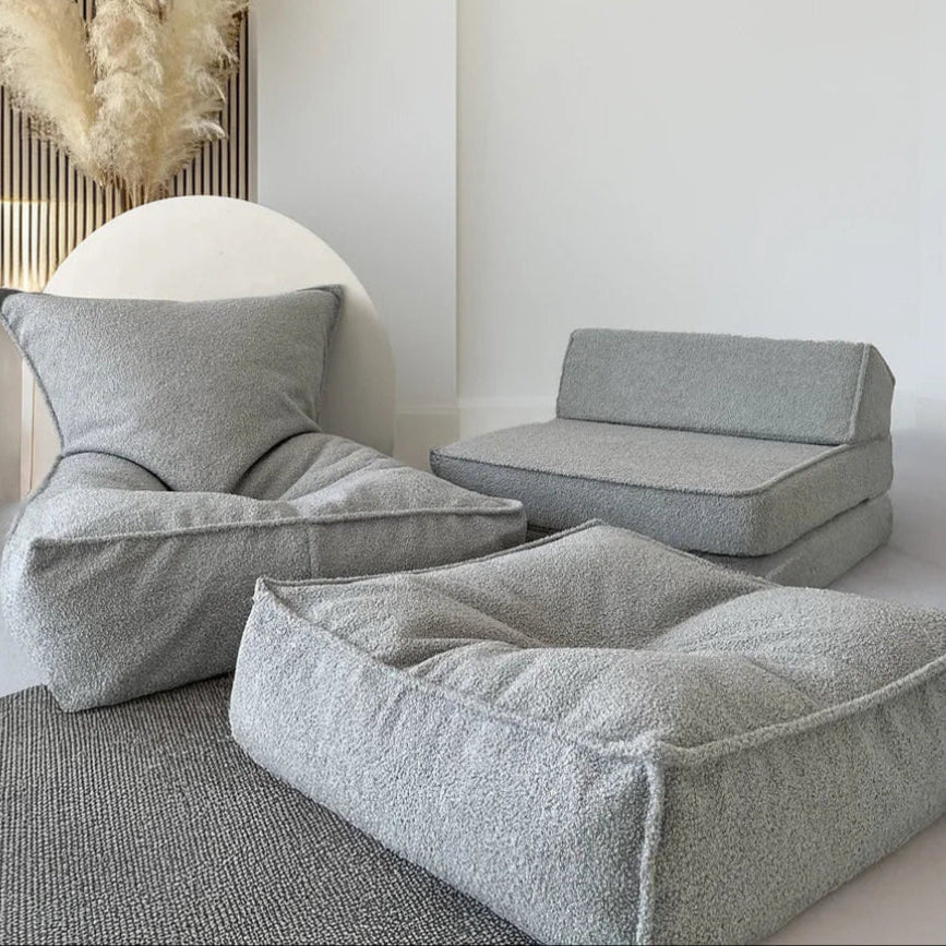 Grijze bouclé ottoman kinderpoef op de voorgrond, met een bijpassende zitzak en lounger op de achtergrond.