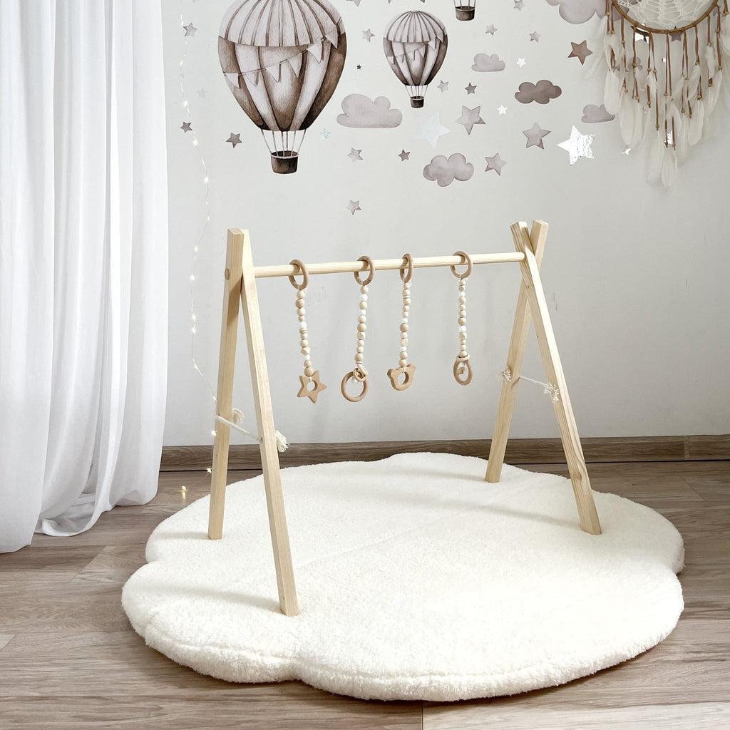 Witte teddy speelmat in wolkvorm met een houten babygym en hangend speelgoed in een kinderkamer.