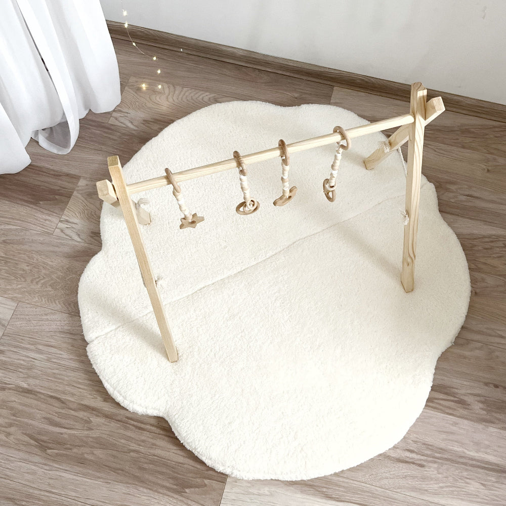 Witte Cloud speelmat van teddy onder een houten babygym, schuin van boven gezien.