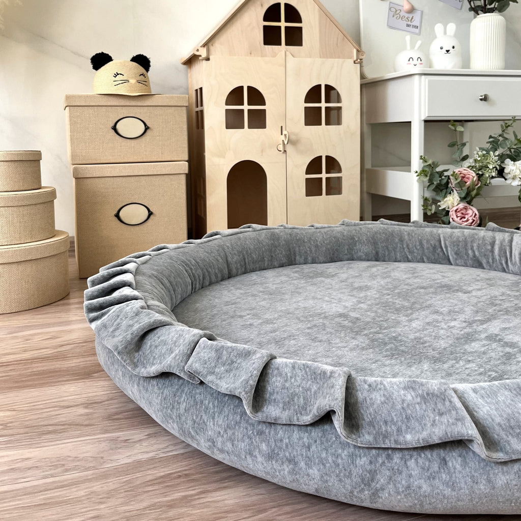 Grijs rond speelnest Soft Velvet met opstaande rand en ruches op een houten vloer in een kinderkamer.
