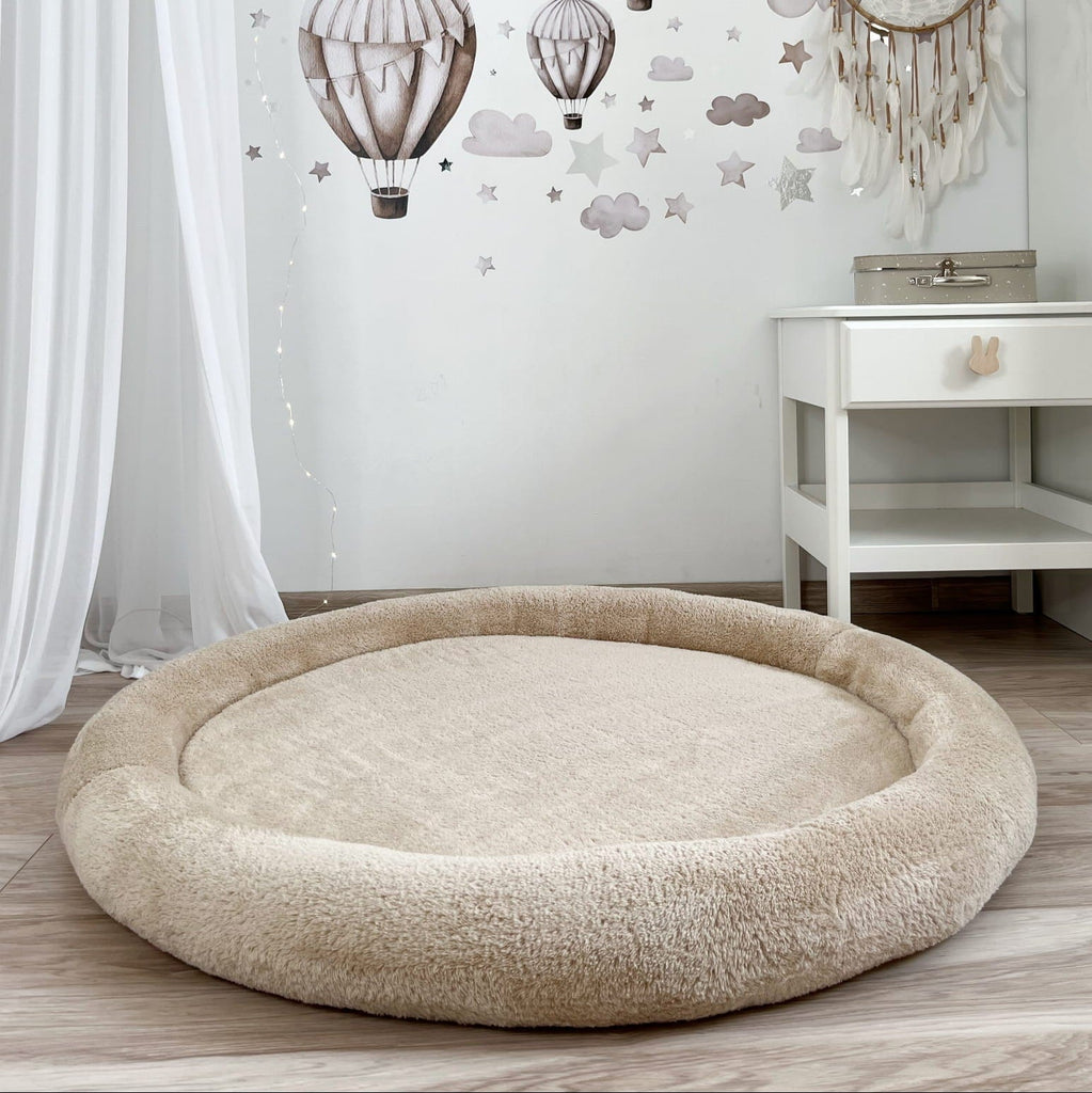 Beige teddy speelnest met opstaande rand op een houten vloer in een kinderkamer met luchtballonnen op de muur