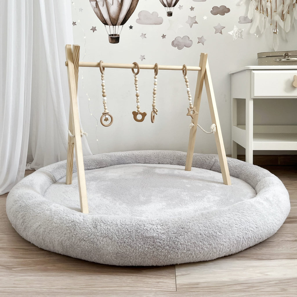 Grijs teddy speelnest met een houten speelboog en hangend speelgoed in een babykamer