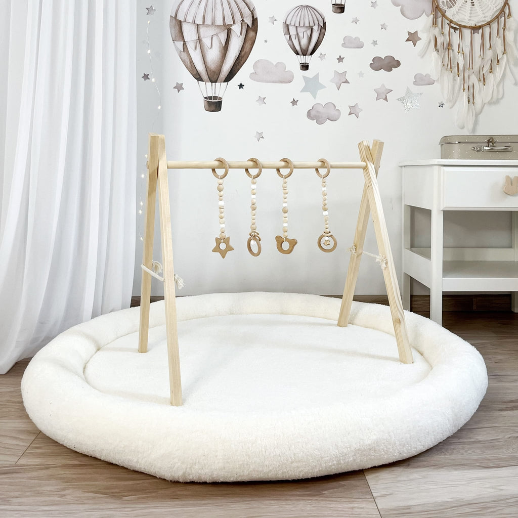 Wit teddy speelnest met een houten speelboog en vier hangende speeltjes in een kinderkamer