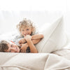 Twee kinderen spelen tussen crèmekleurige bouclé zitzakken, met een rugleuning tussen hen in.